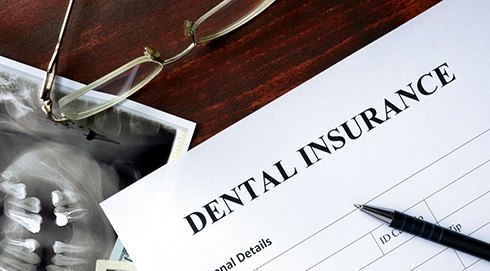 Corner of a “Dental Insurance” form with a pen and glasses on a desk