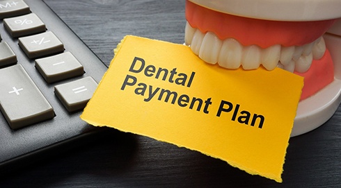 Set of dentures holding a yellow paper that reads, “Dental Payment Plan”