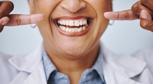 a person pointing at their teeth and smiling