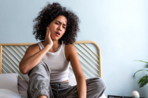 Woman waking up to jaw pain and rubbing the ache